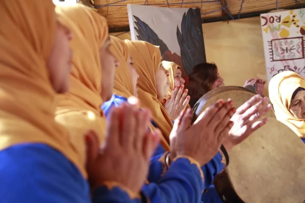 Femmes en tenue jaune et bleue frappant dans leurs mains autour d’un bendir
